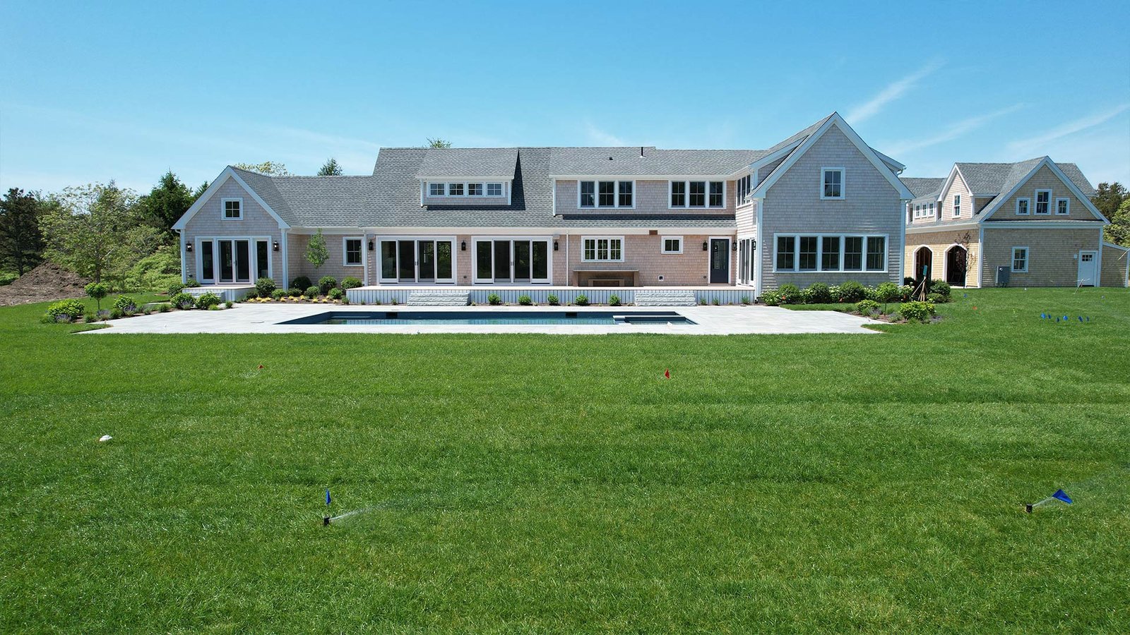 Full rear lawn view with irrigation active, pool surround and cedar shingle estate — West Tisbury Martha's Vineyard